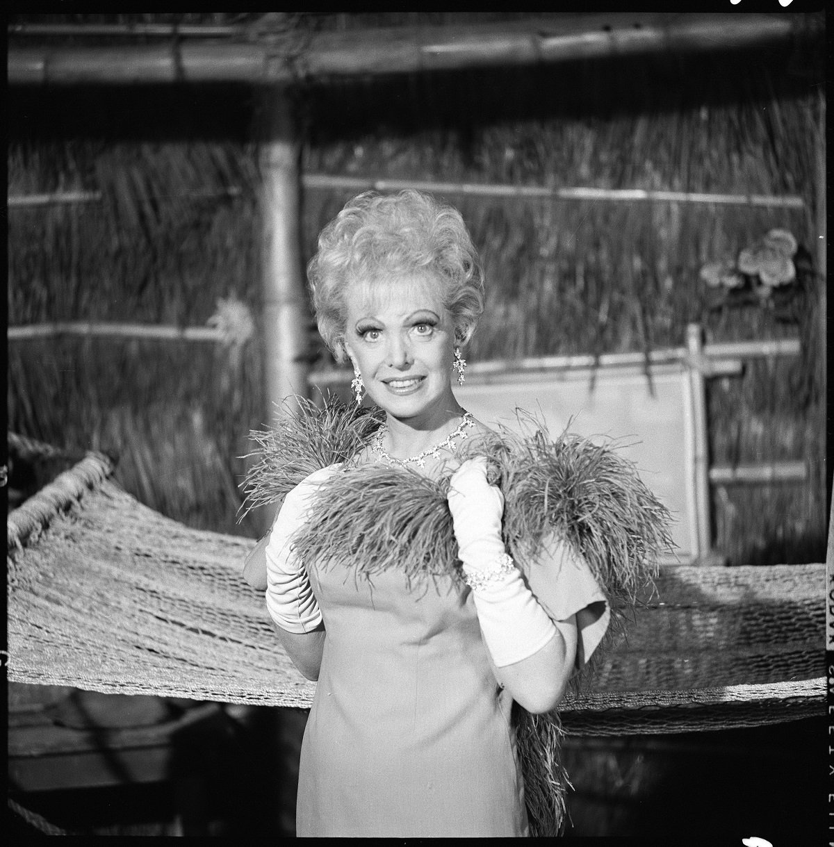 'Gilligan's Island' star Natalie Schafer in a dress and boa poses in a hut for a black and white promotional photo.