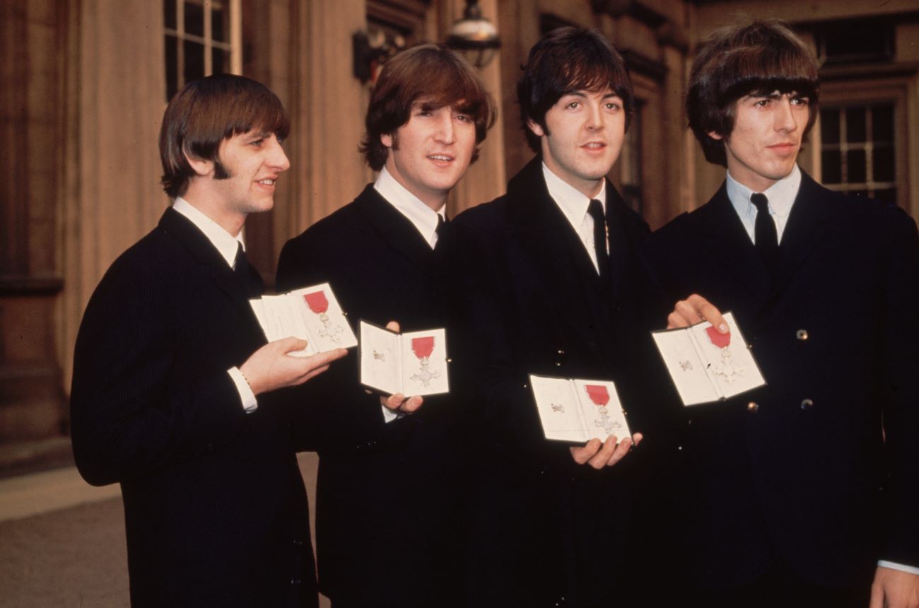 Ringo Starr, John Lennon, Paul McCartney, and George Harrison pose with medals after receiving their MBEs from the queen.