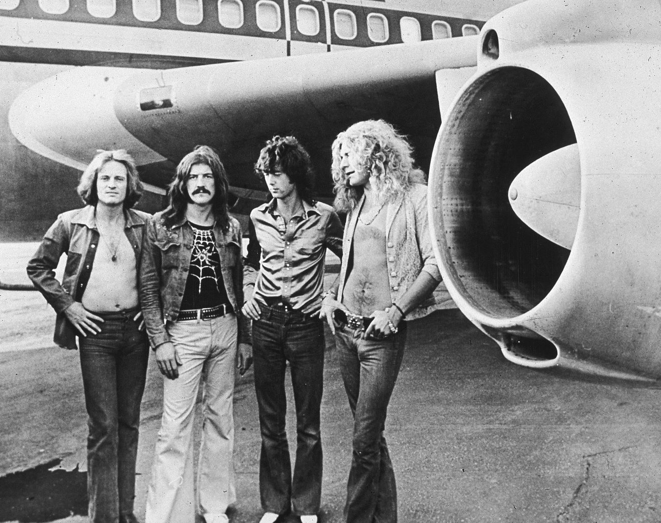 A black and white picture of Led Zeppelin posing in front of a plane.