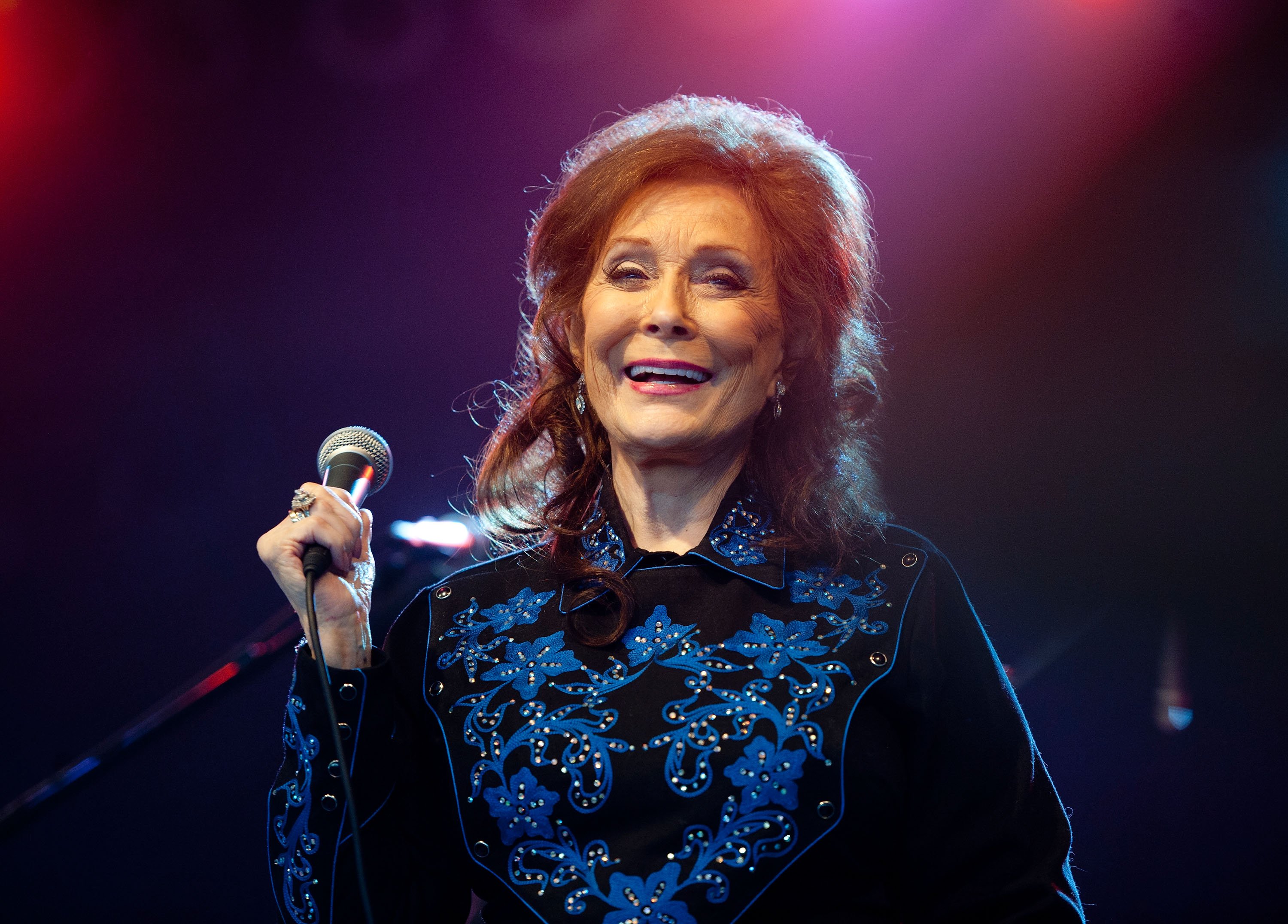 Loretta Lynn smiles while holding up a microphone