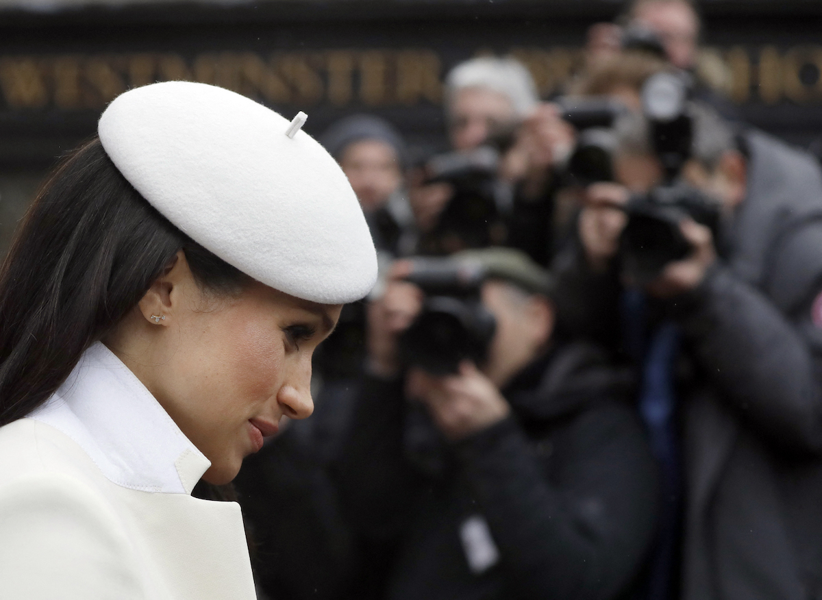 Meghan Markle, the subject of a 2016 statement which Prince Harry claimed in 'Spare' made King Charles and Prince William 'furious', looks on wearing a white outfit as photographers stand in the background