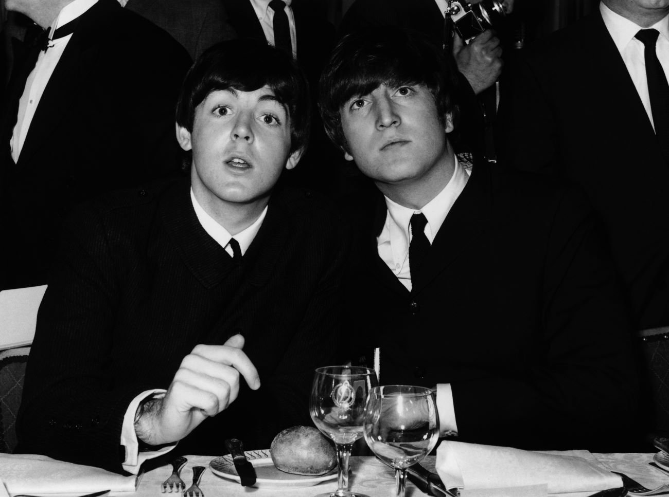 Paul McCartney and John Lennon sit at a table together.