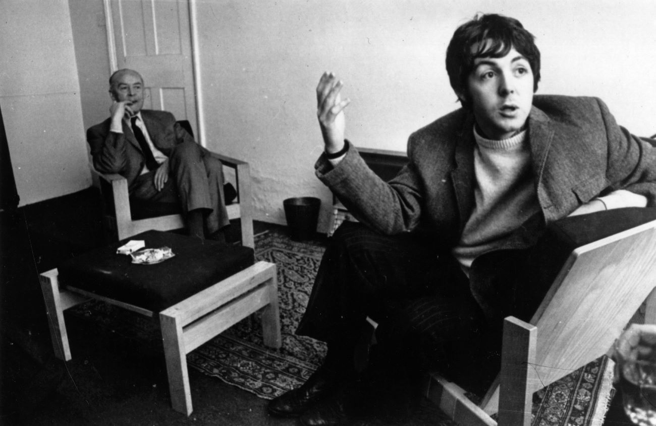 A black and white picture of Paul McCartney and his dad, Jim, sitting in wooden chairs.