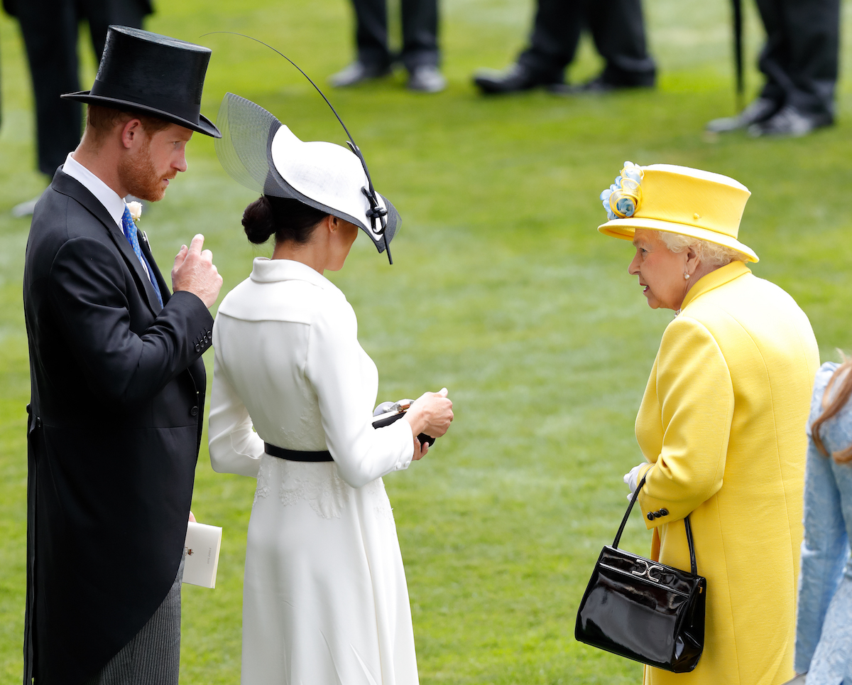 Prince Harry, who claimed in 'Spare' Meghan Markle mistook Prince Andrew for Queen Elizabeth II's assistant, stands with Meghan Markle and Queen Elizabeth II.