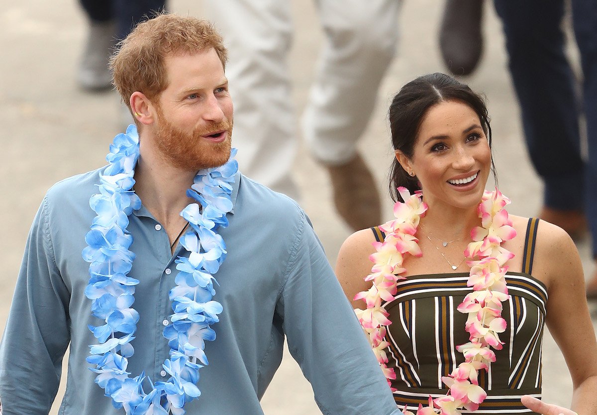 Prince Harry and Meghan Markle smile with flower leis around their necks.