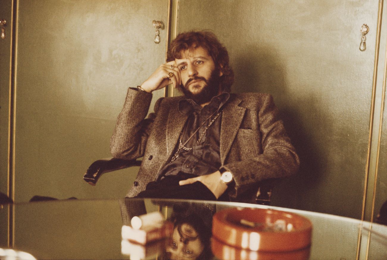 Ringo Starr sits at a table with his head leaning on his hand.