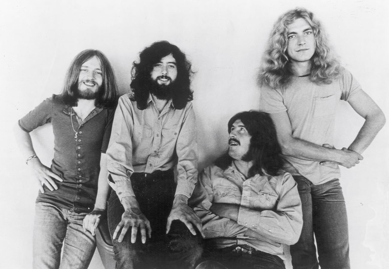 A black and white picture of John Paul Jones, Jimmy Page, John Bonham, Robert Plant of Led Zeppelin posing against a wall.