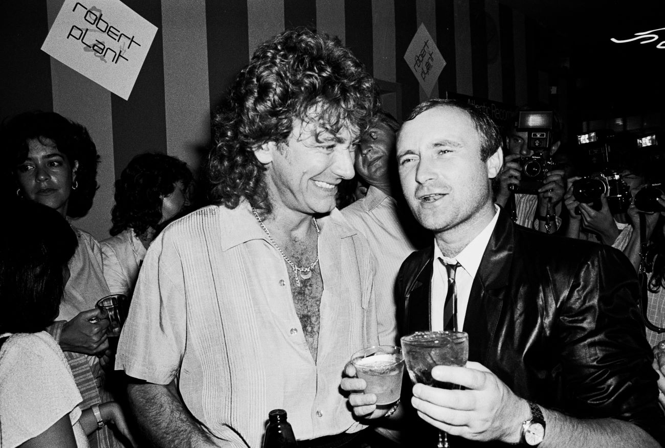 A black and white picture of Robert Plant and Phil Collins holding drinks.