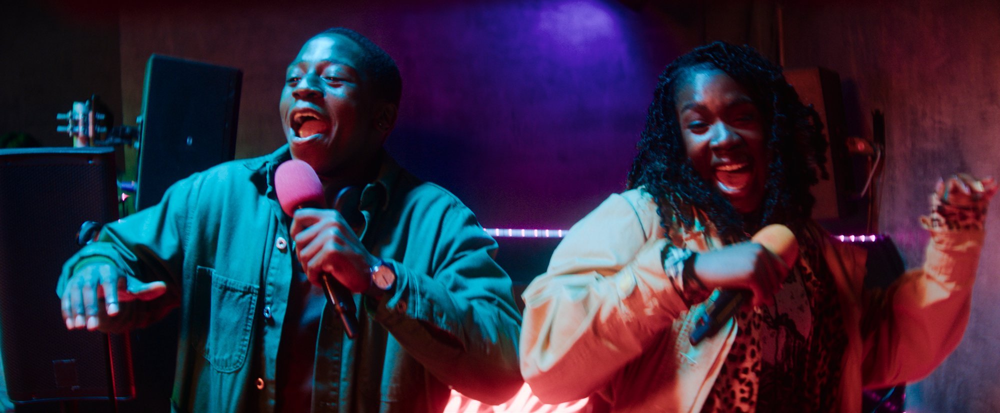 'Rye Lane' David Jonsson as Dom and Vivian Oparah as Yas (1) singing into microphones while dancing