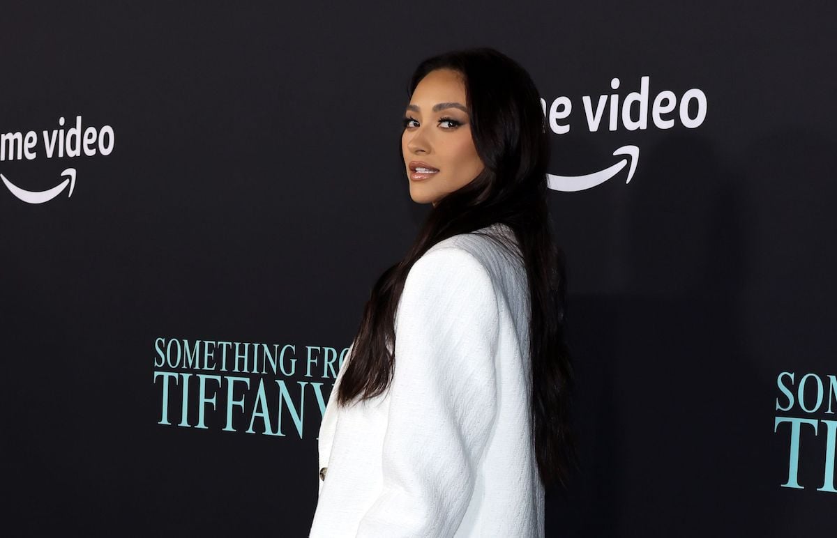 manifestation guru Shay Mitchell in a white suit looks over her shoulder on the red carpet