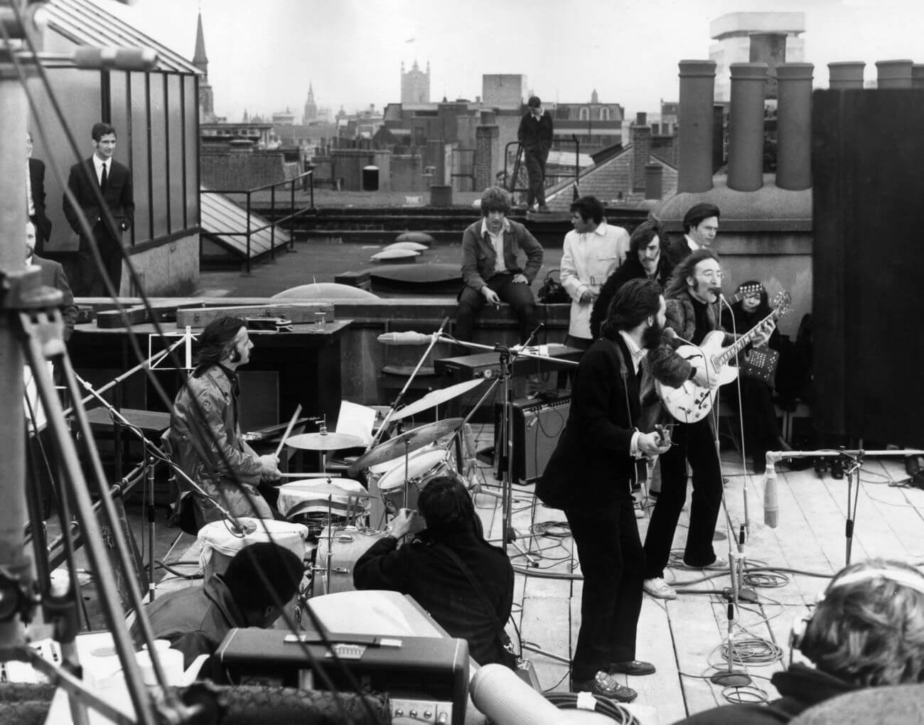 A black and white picture of The Beatles playing a concert on a rooftop while a small crowd watches, as seen in The Beatles: Get Back. 