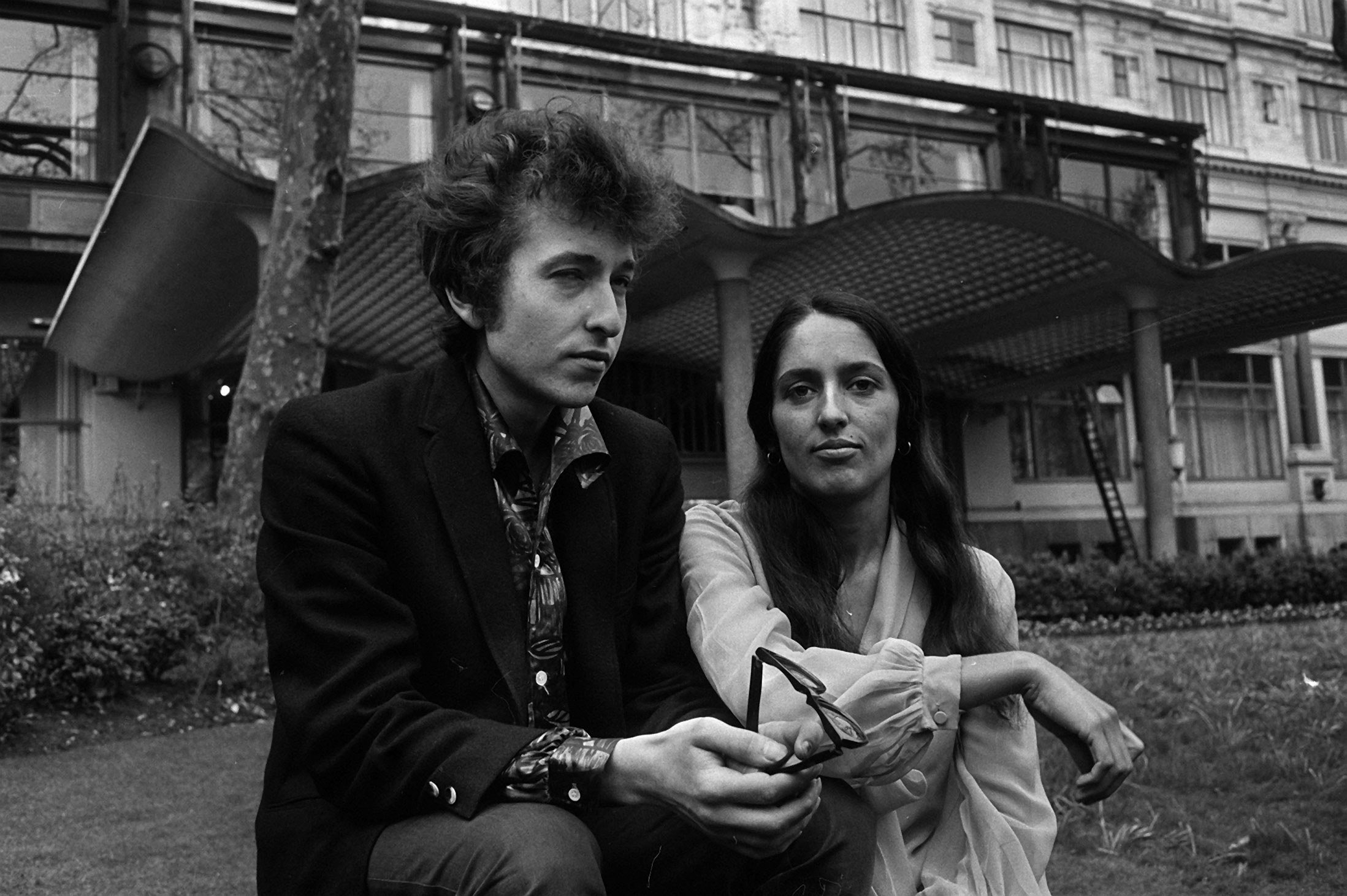 A black and white picture of Bob Dylan and Joan Baez sitting in front of a building.