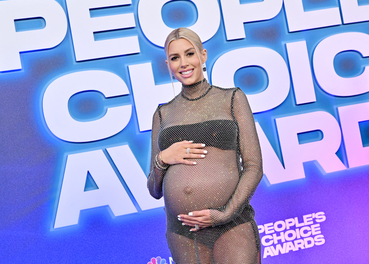 Heather Rae Young poses holding her baby bump at an event.