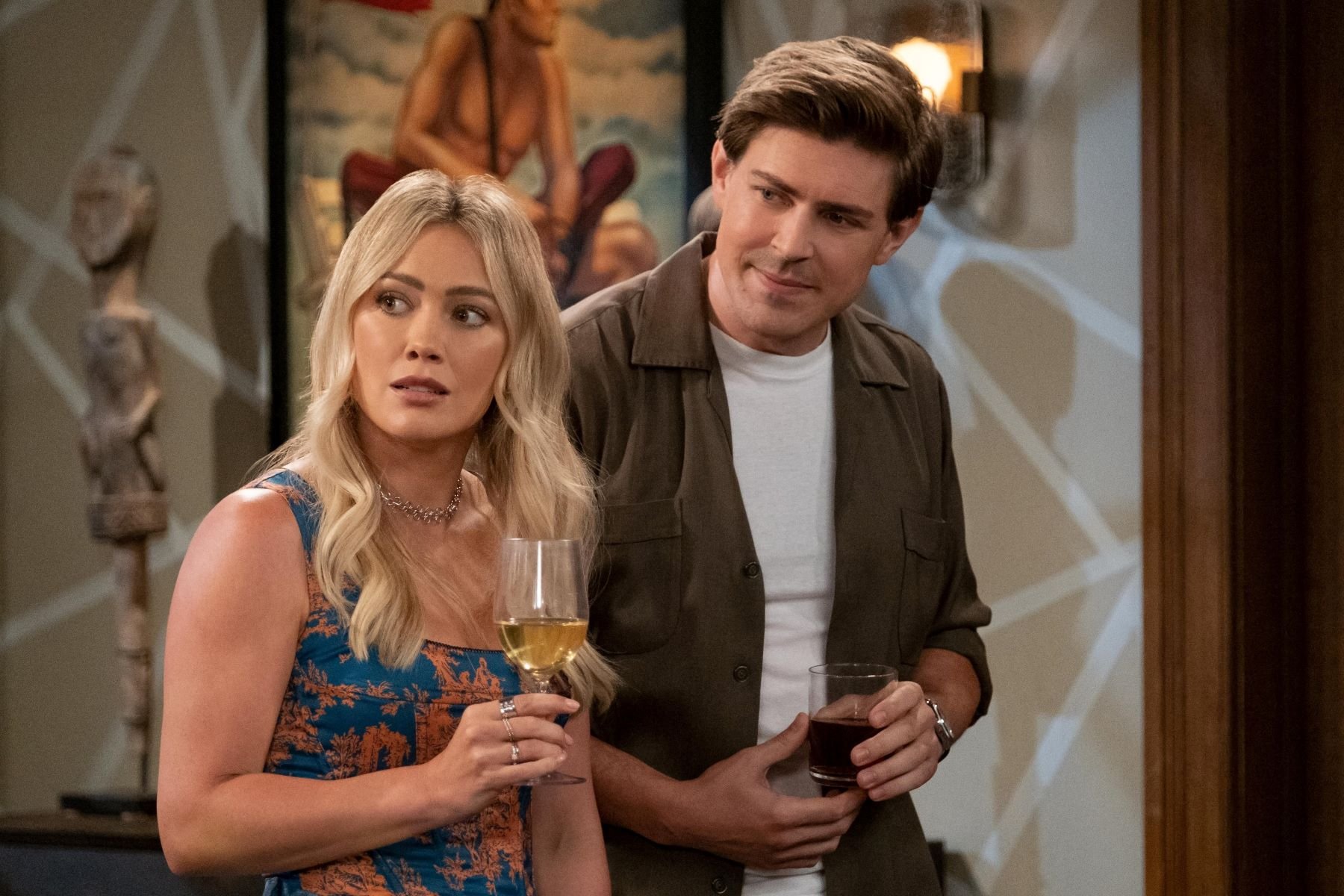 Hilary Duff as Sophie and Chris Lowell as Jesse in 'How I Met Your Father' Season 2 Episode 3, 'The Reset Button.' Sophie wears a blue and orange tank top. Jesse wears a dark brown button-up shirt over a white shirt.