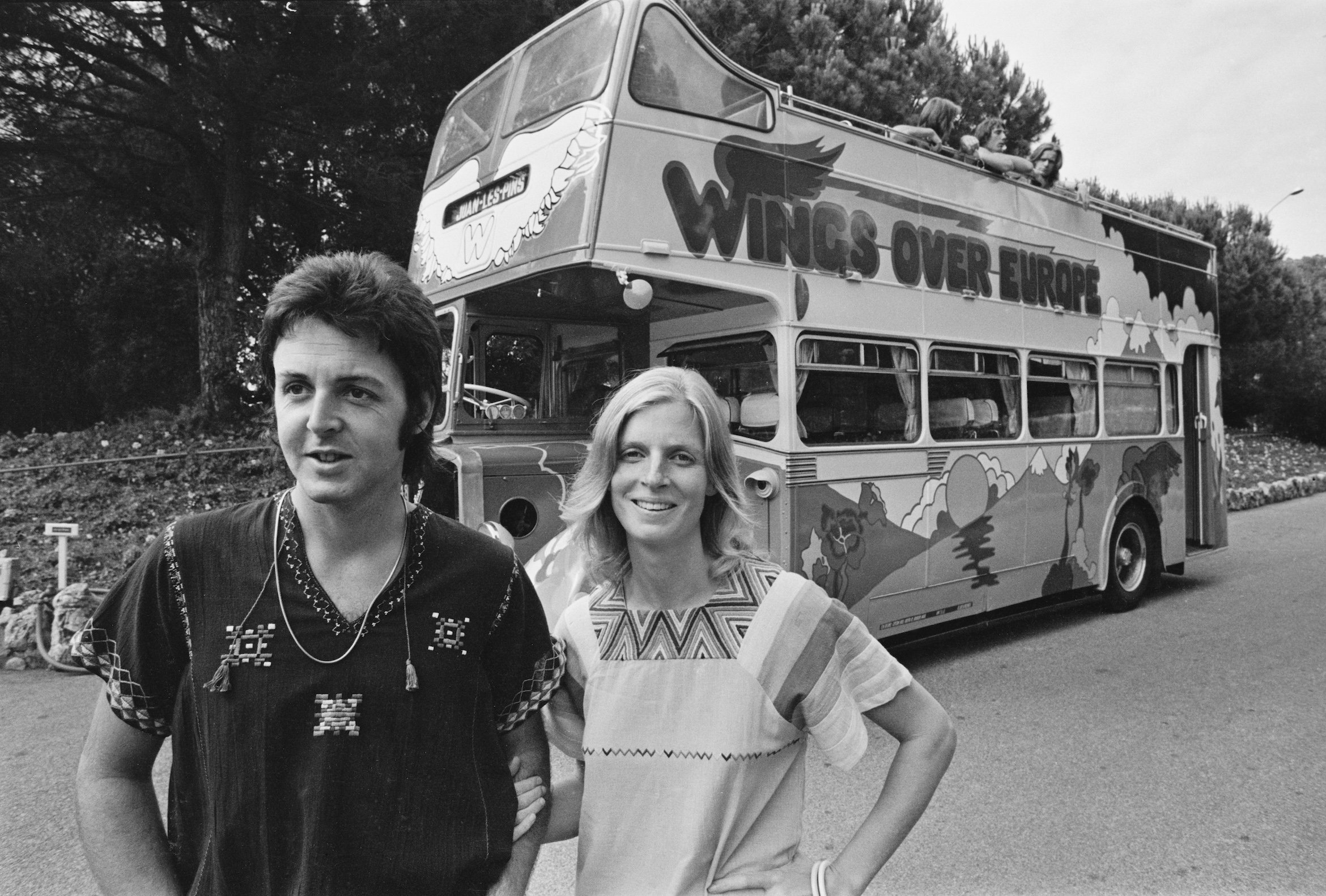 Paul McCartney and Linda McCartney stand in front of their Wings Over Europe tour bus