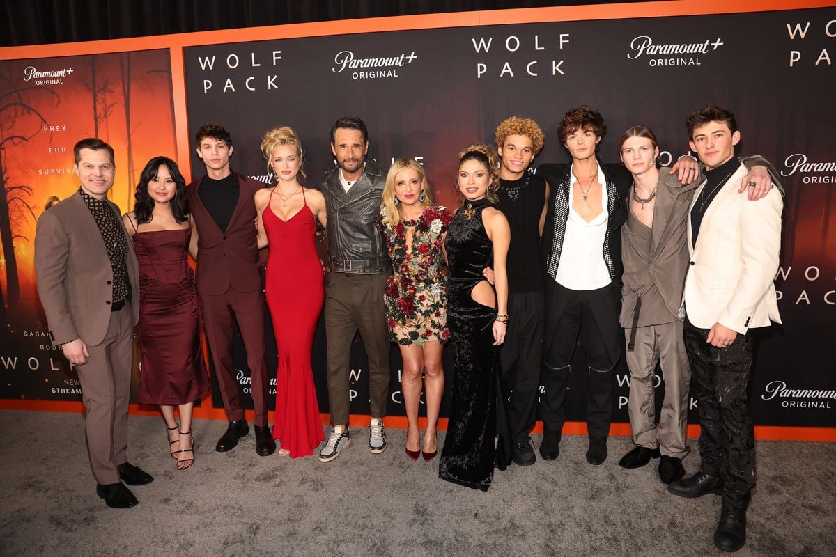 The cast of "Wolf Pack" poses in front of a backdrop featuring the logo for the series.