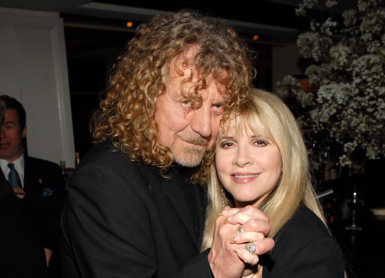 Robert Plant and Stevie Nicks hold hands and pose cheek to cheek.