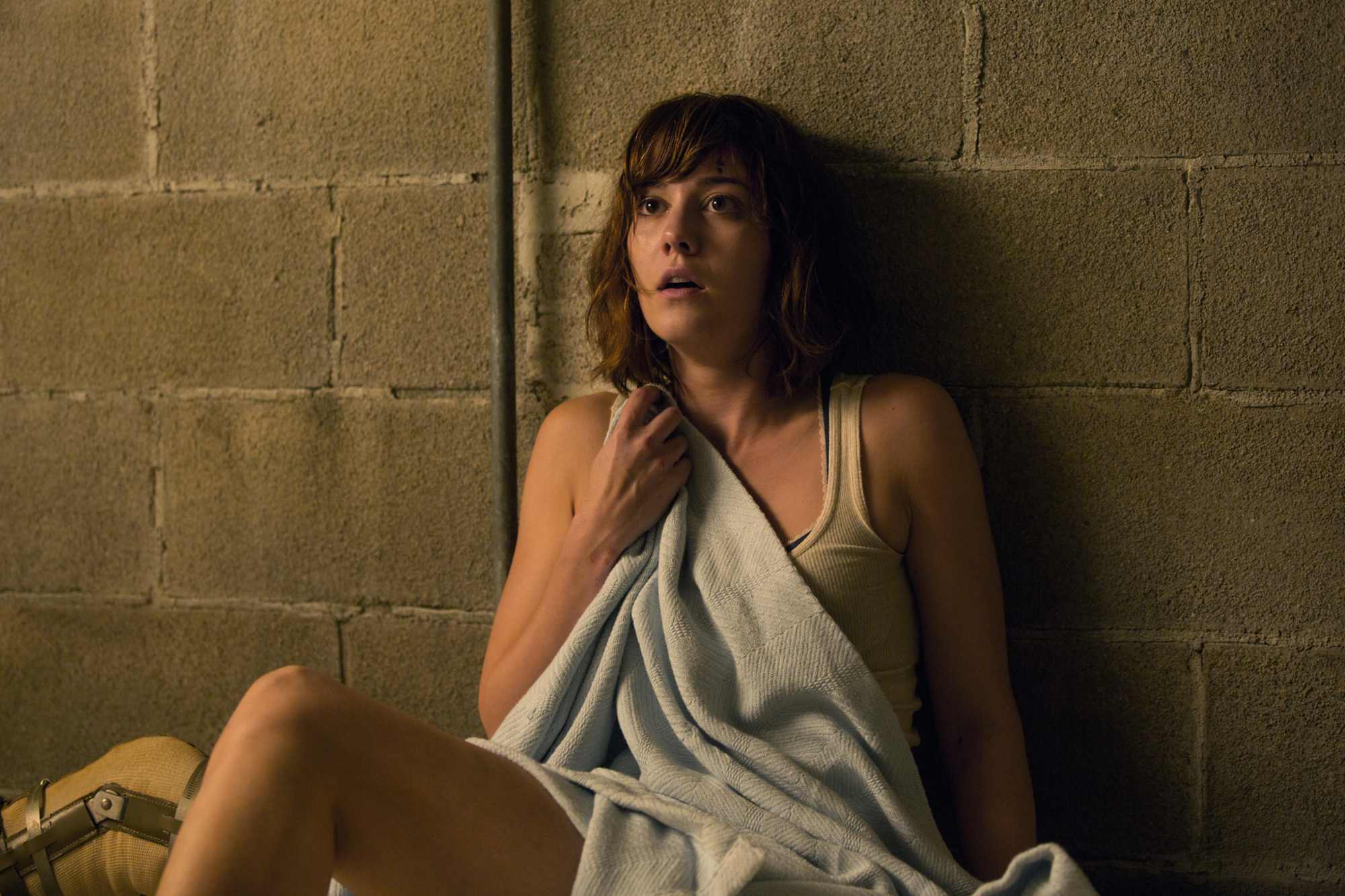 '10 Cloverfield Lane' Mary Elizabeth Winstead as Michelle looking terrified with her back against a wall, holding onto a blanket.