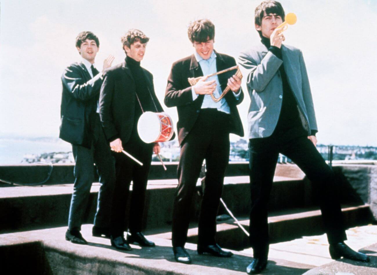 Paul McCartney, Ringo Starr, John Lennon, and George Harrison play small instruments on a rooftop.