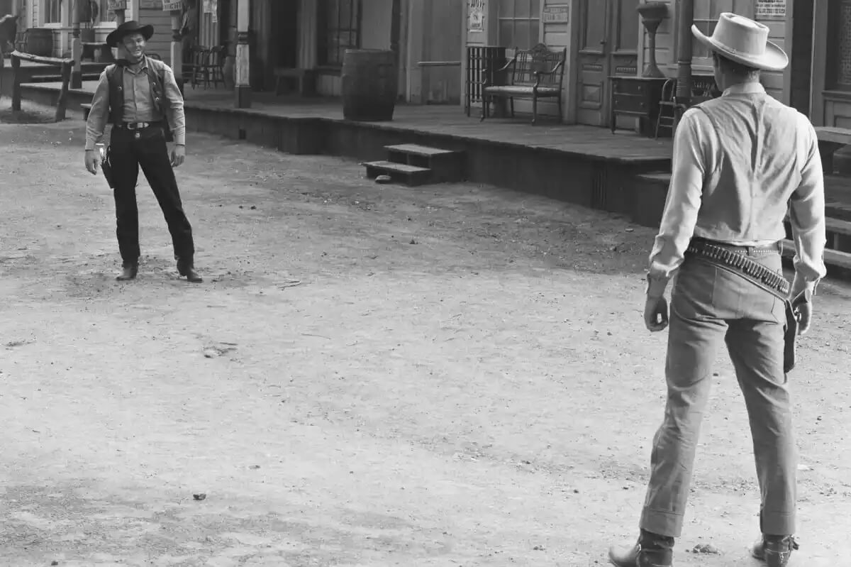 'Gunsmoke' James Arness as Matt Dillon in a gunfight on a street opposite a black-hatted villain.