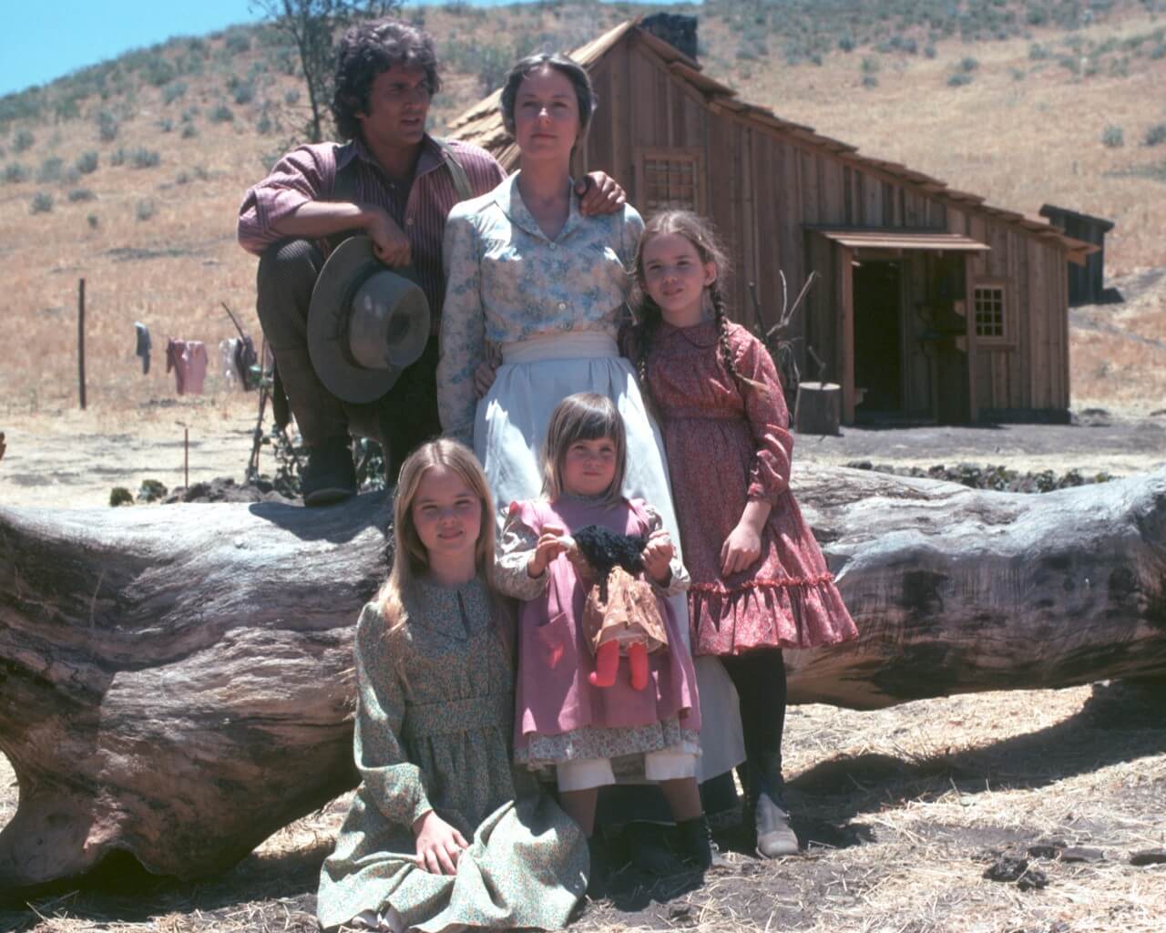 The cast of 'Little House on the Prairie' poses in front of the log house. 