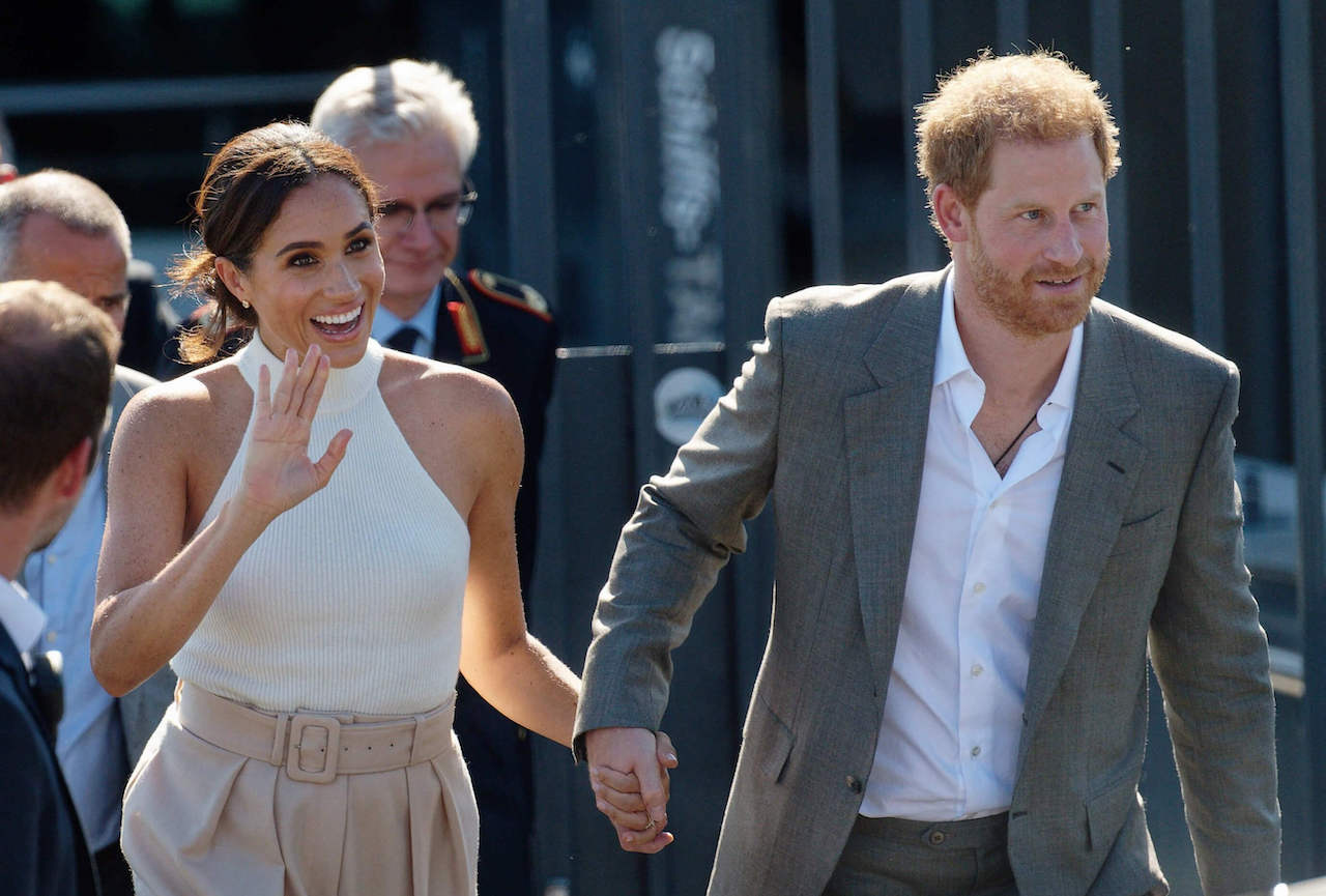 Meghan Markle waves and holds hands with Prince Harry in 2022.