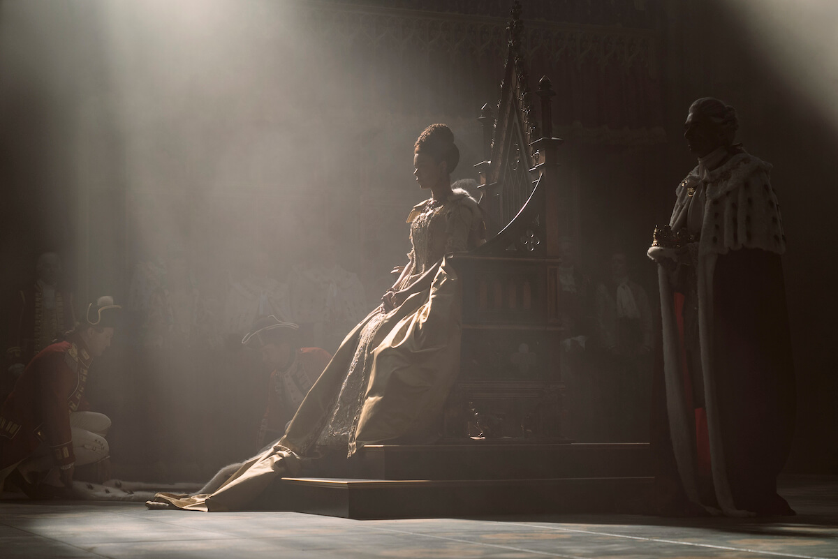 India Amarteifio as Young Queen Charlotte sitting in a dark throne room in 'Queen Charlotte: A Bridgerton Story