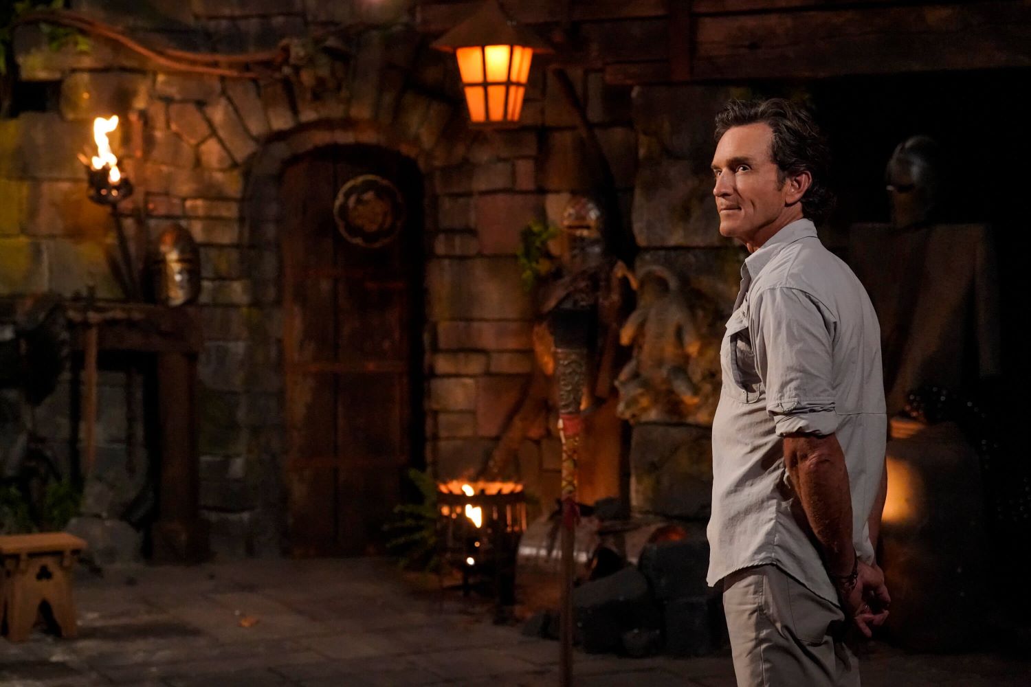 Jeff Probst, the host of 'Survivor' Season 44, attends Tribal Council wearing a light gray button-up shirt with rolled-up sleeves and gray pants.