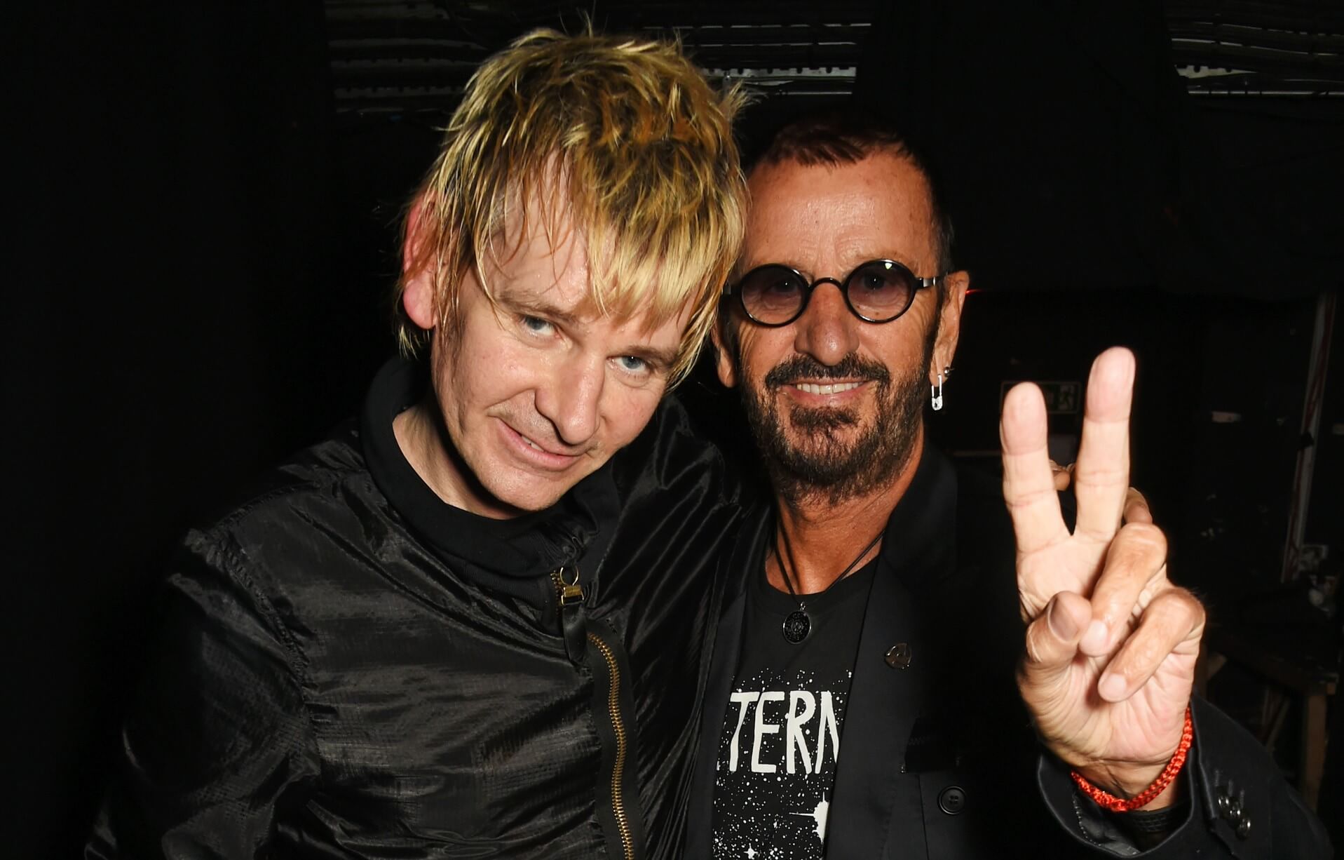 Zak Starkey stands with Ringo Starr, who holds up a peace sign.