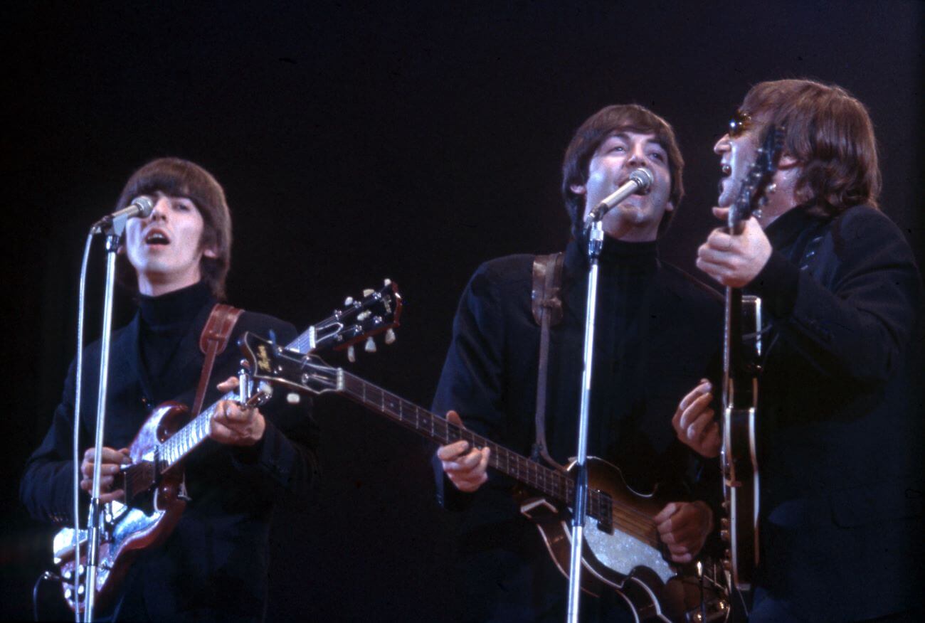 George Harrison, Paul McCartney, and John Lennon play guitars and sing into microphones. 