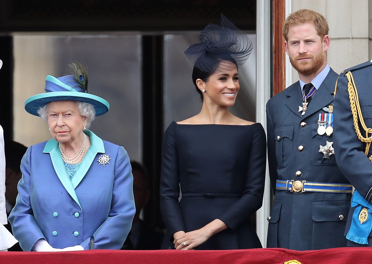 Queen Elizabeth II, Meghan Markle, and Prince Harry standing on the balcony of Buckingham Palace to mark the Centenary of the RAF