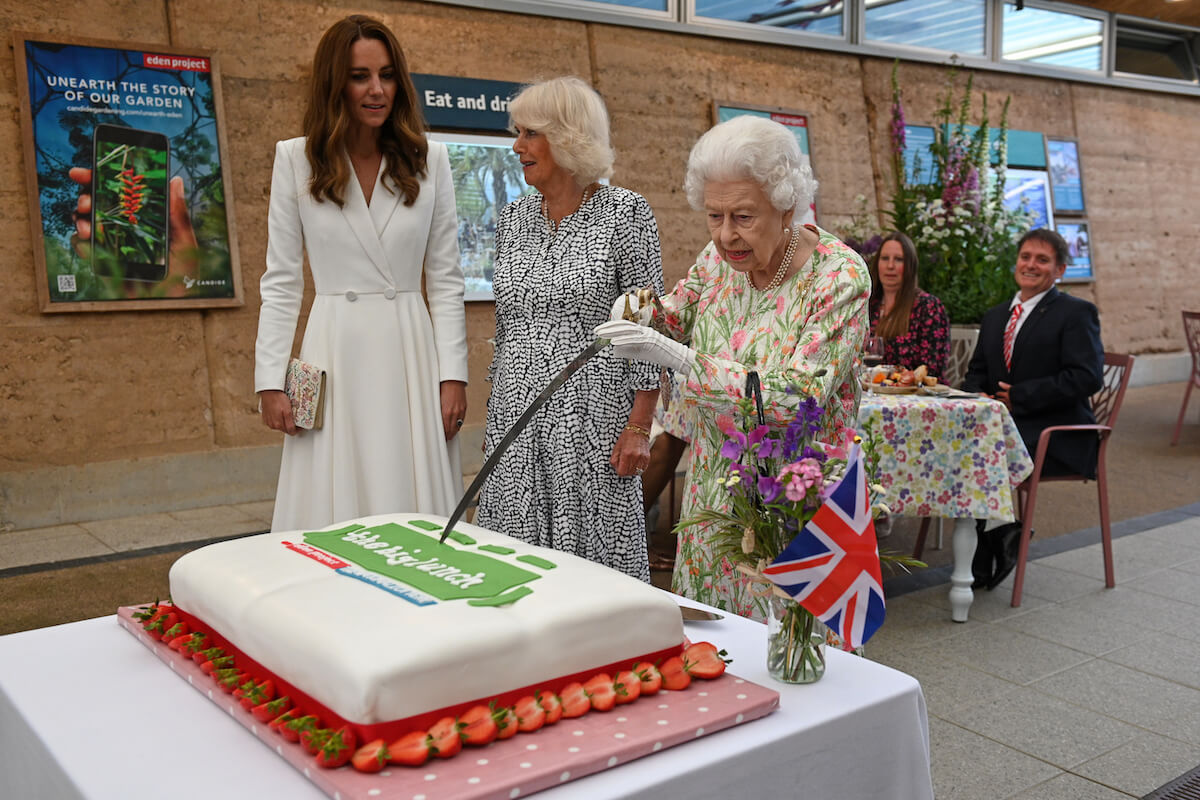 Queen Elizabeth cuts a cake with a sword as Kate Middleton and Camilla Parker Bowles, who reacted differently per a body language expert, look on