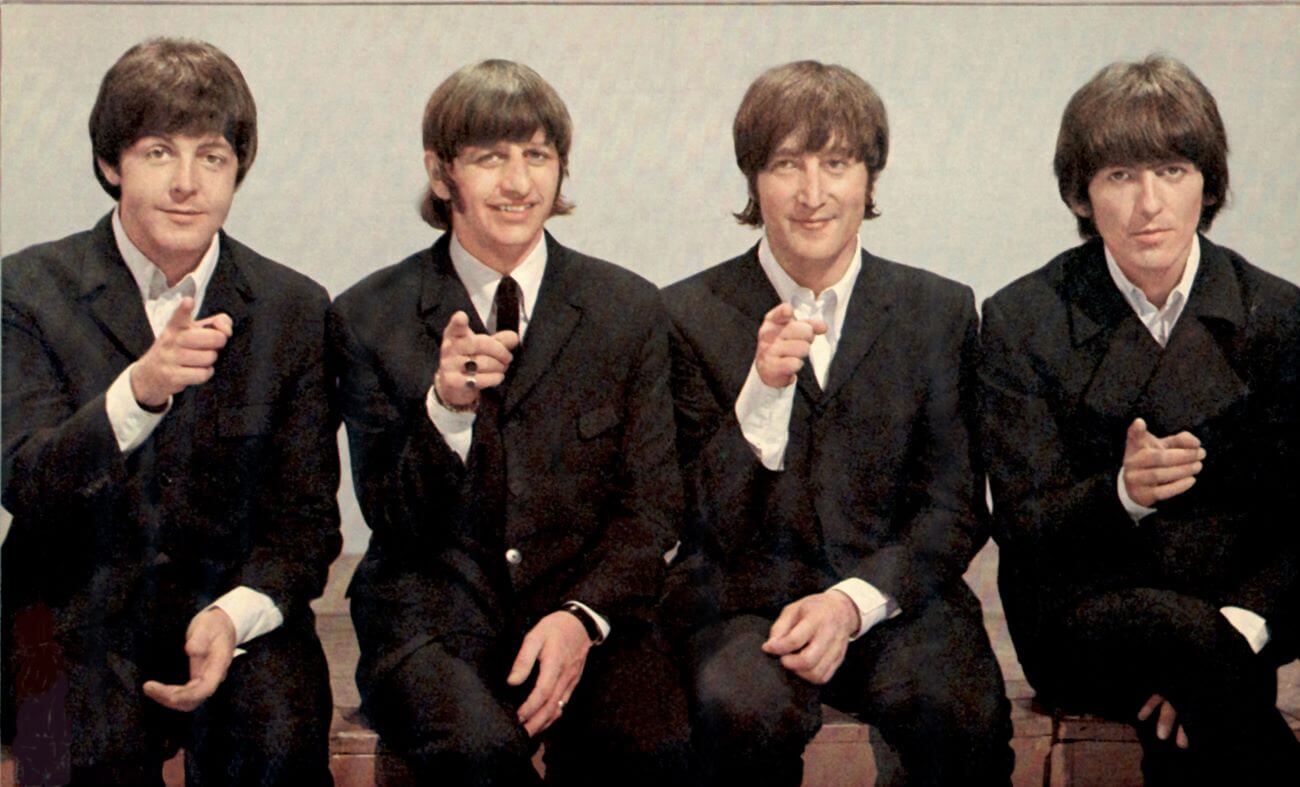 The Beatles wear suits and point at the camera.