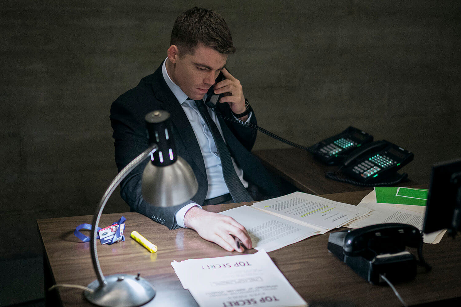 The Night Agent: Gabriel Basso as Peter Sutherland on a phone call at the Night Action desk while looking at documents