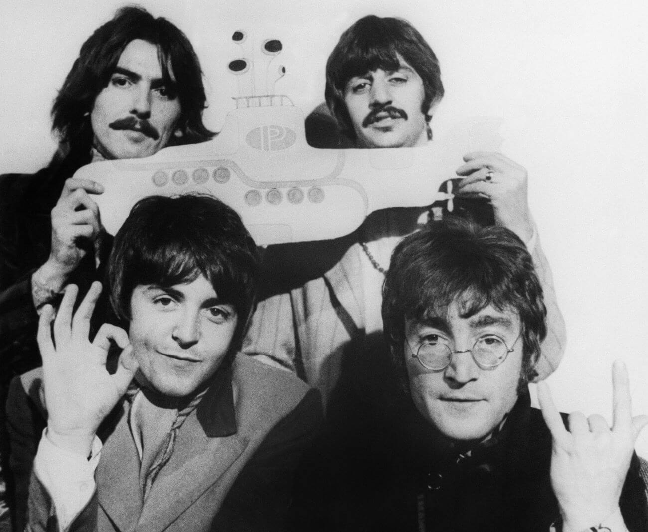 A black and white picture of George Harrison, Ringo Starr, Paul McCartney, and John Lennon of The Beatles posing with a yellow submarine cut out.