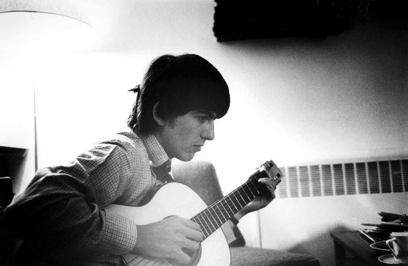 A black and white picture of George Harrison sitting and holding an acoustic guitar.