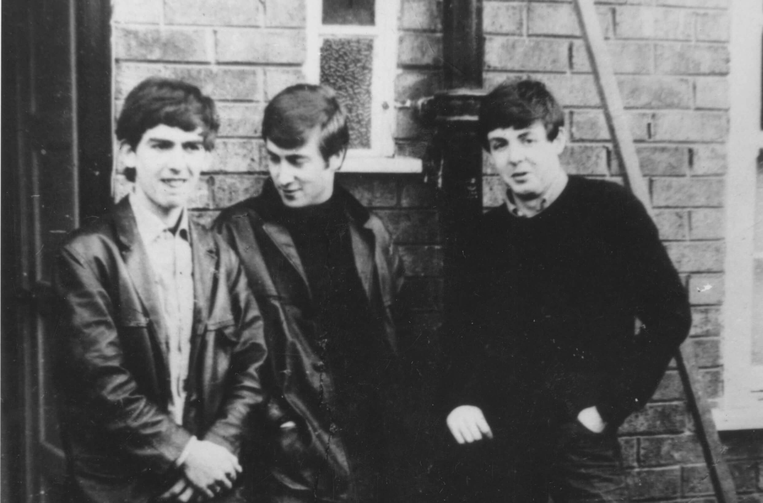 A black and white picture of George Harrison, John Lennon, and Paul McCartney of The Beatles posing against a brick wall.