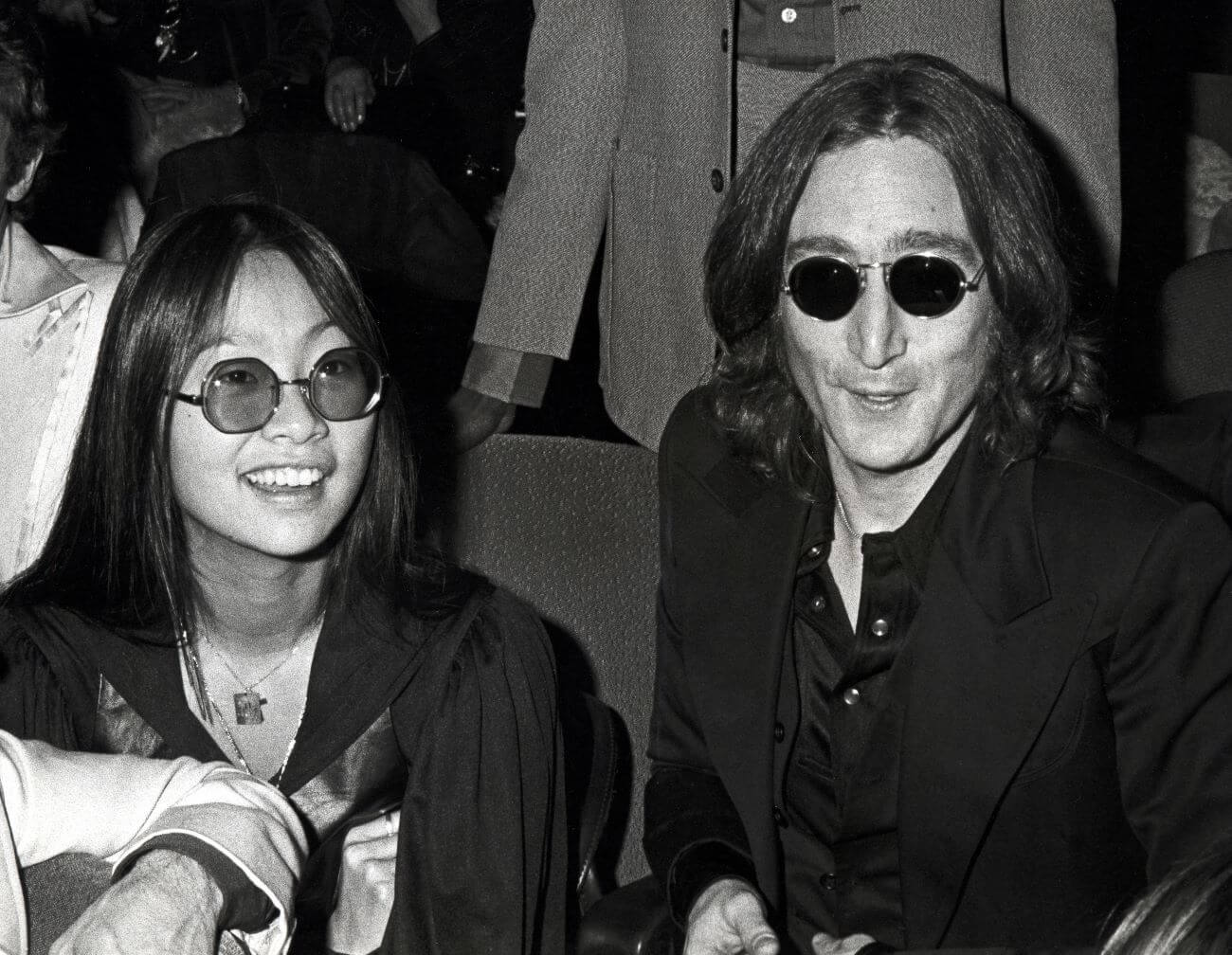 A black and white picture of May Pang and John Lennon sitting together wearing sunglasses.