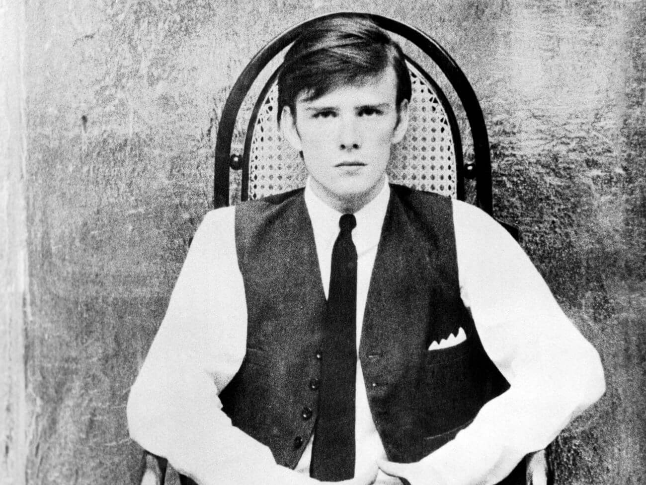 A black and white picture of Stuart Sutcliffe sitting in a chair.