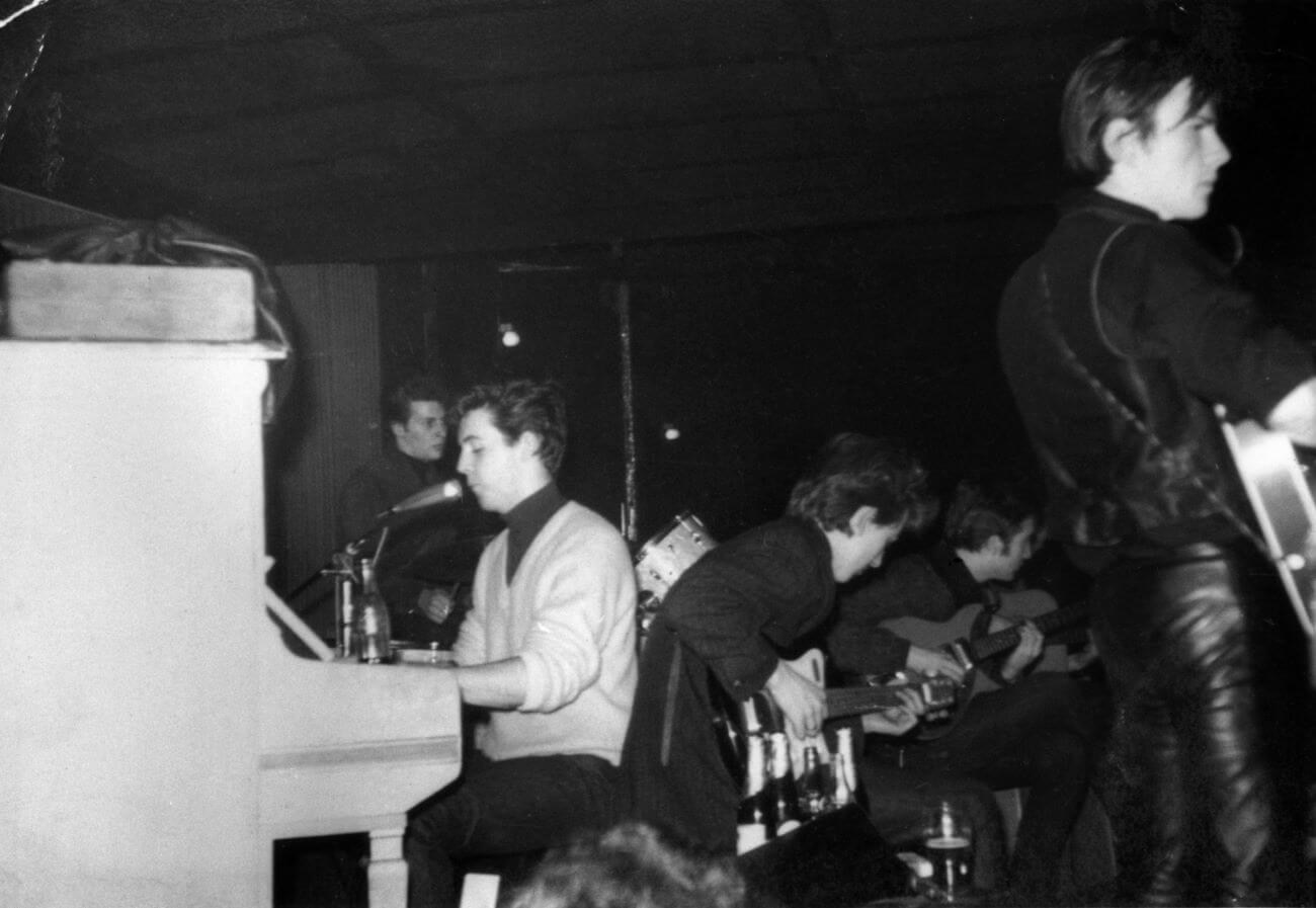 A black and white picture of Paul McCartney playing piano while Stuart Sutcliffe plays guitar.