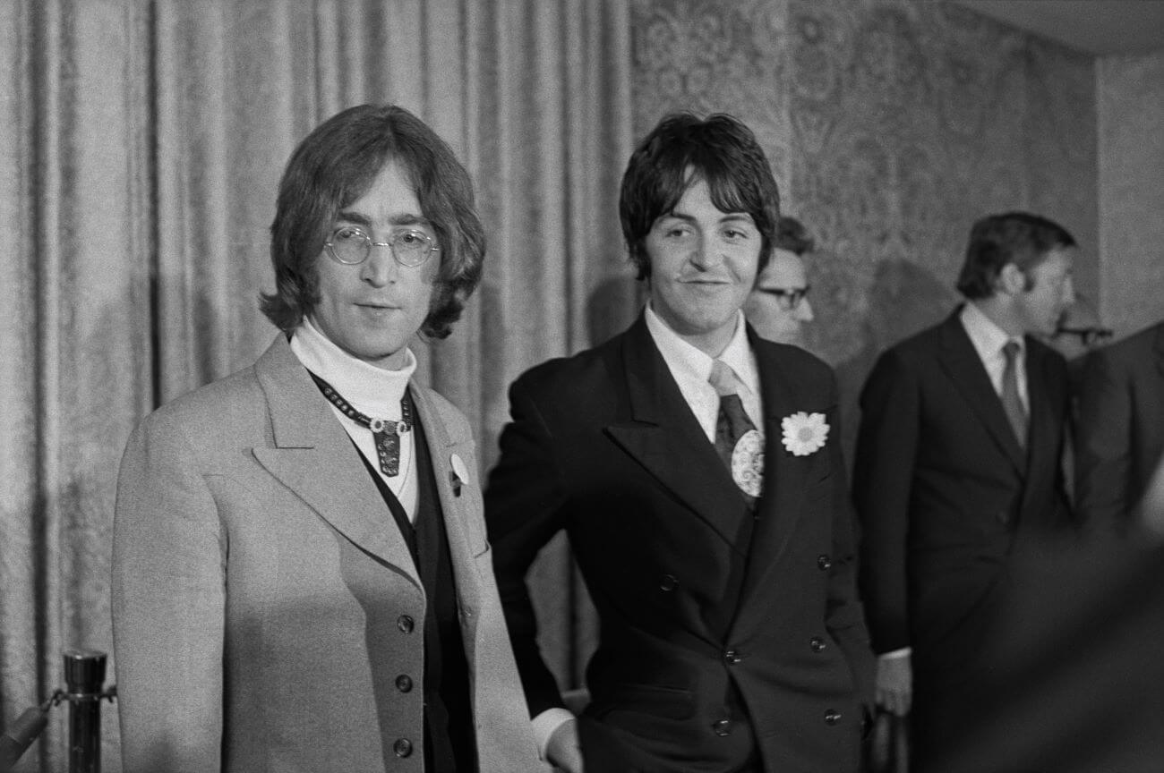 A black and white picture of John Lennon and Paul McCartney wearing suits and standing next to each other.