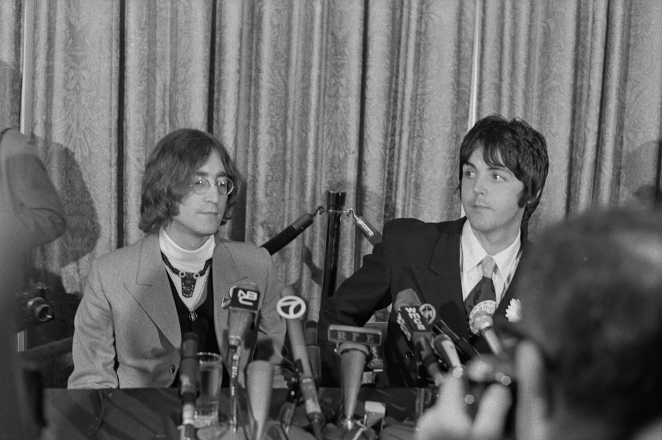 A black and white picture of John Lennon and Paul McCartney sitting at a table in front of microphones.