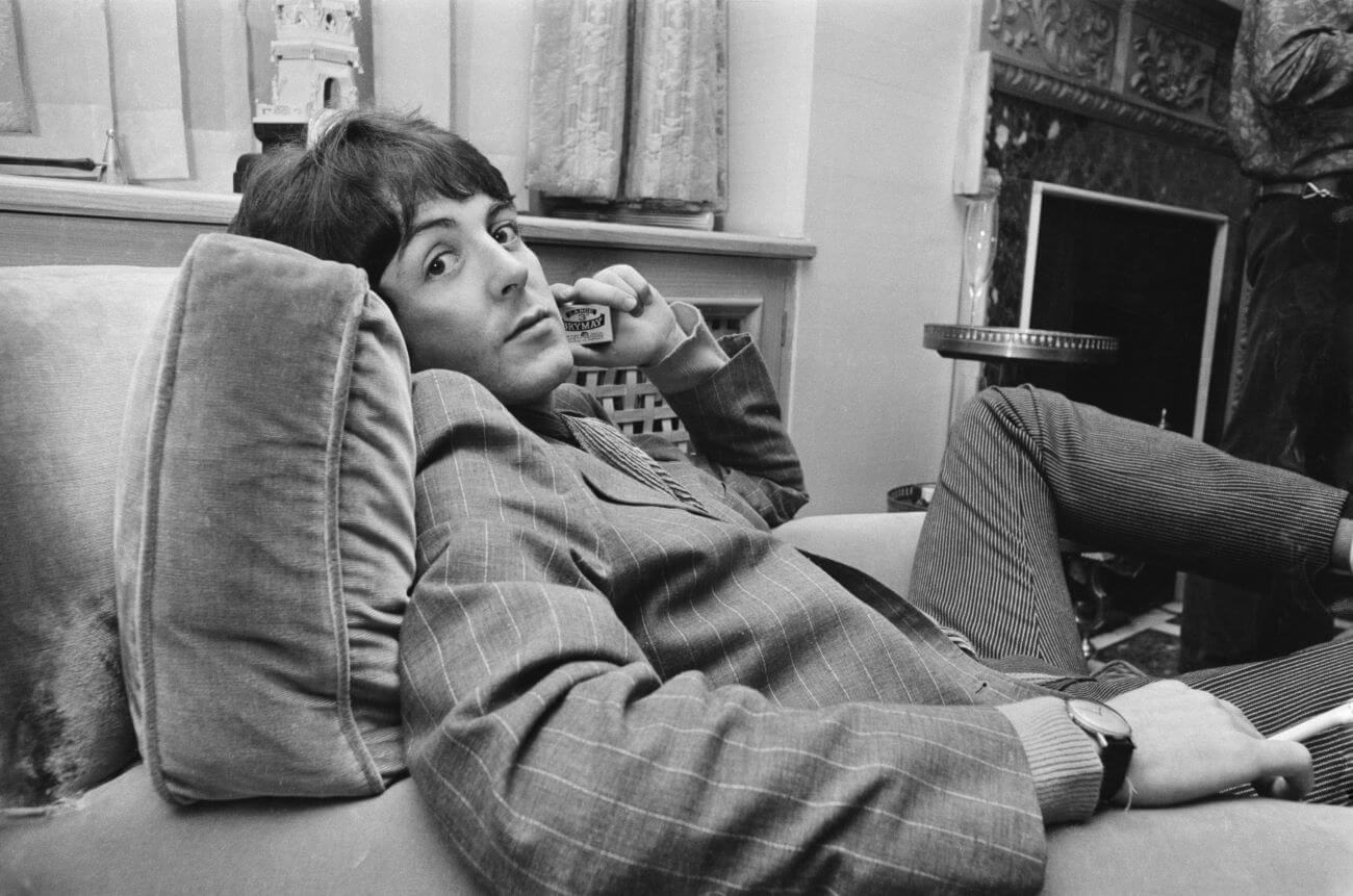 A black and white picture of Paul McCartney sitting in an armchair and holding a pack of matches up to his face.