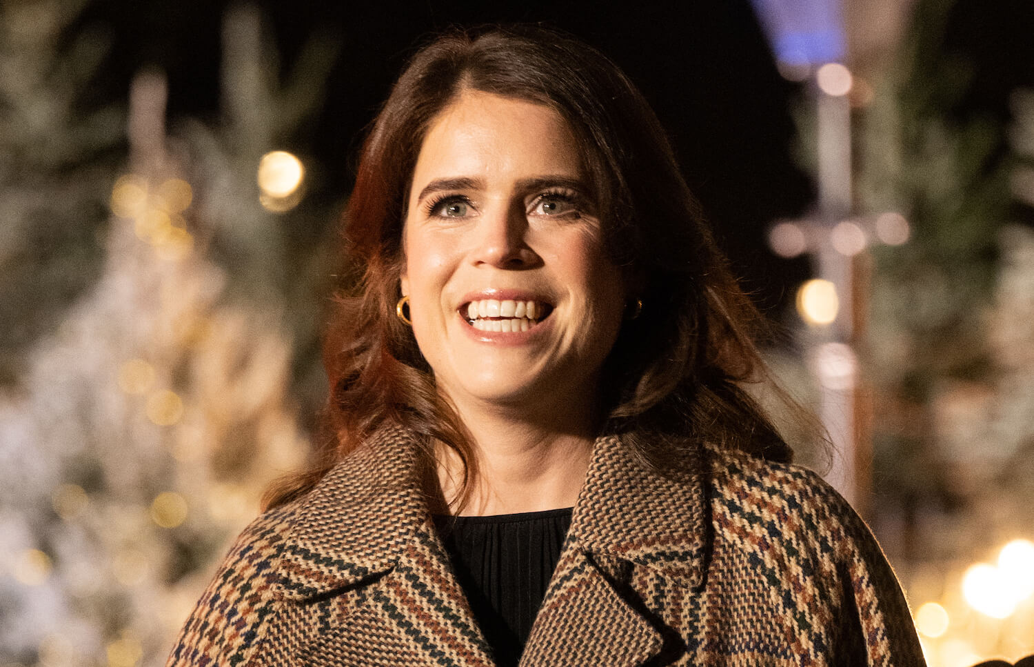 Princess Eugenie smiling in a plaid coat at night