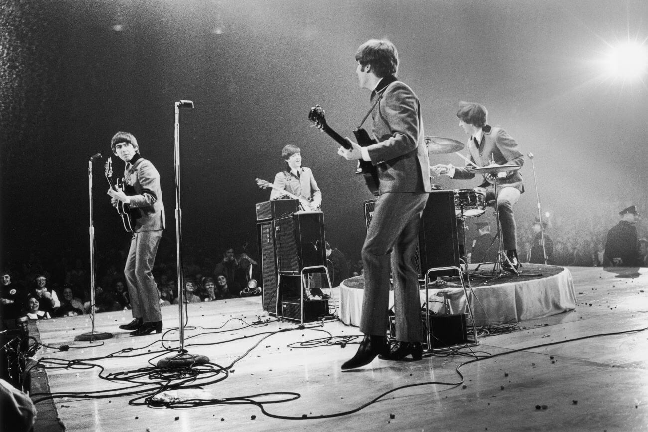 A black and white picture of The Beatles onstage in the middle of a performance.