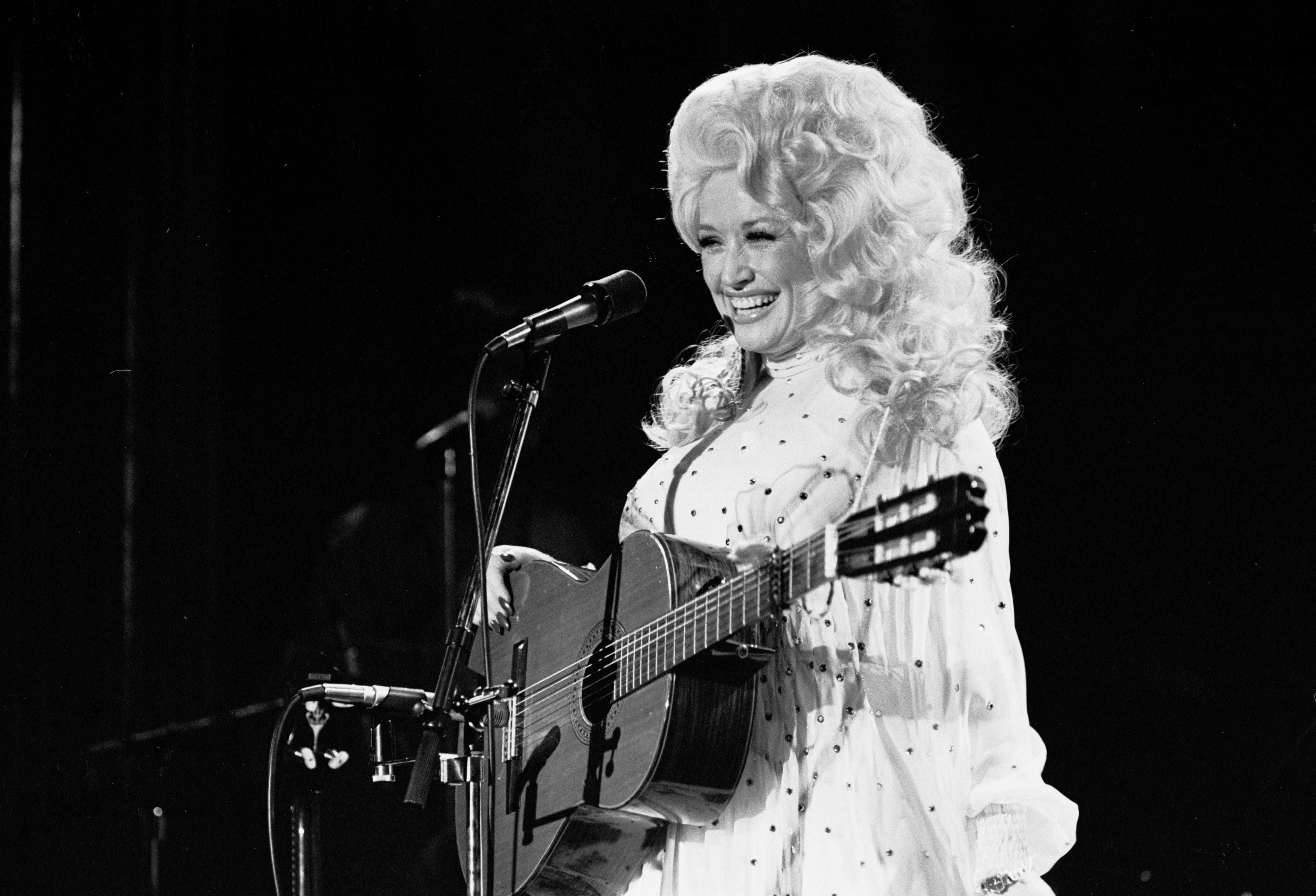 Dolly Parton, singing and playing guitar in black and white.