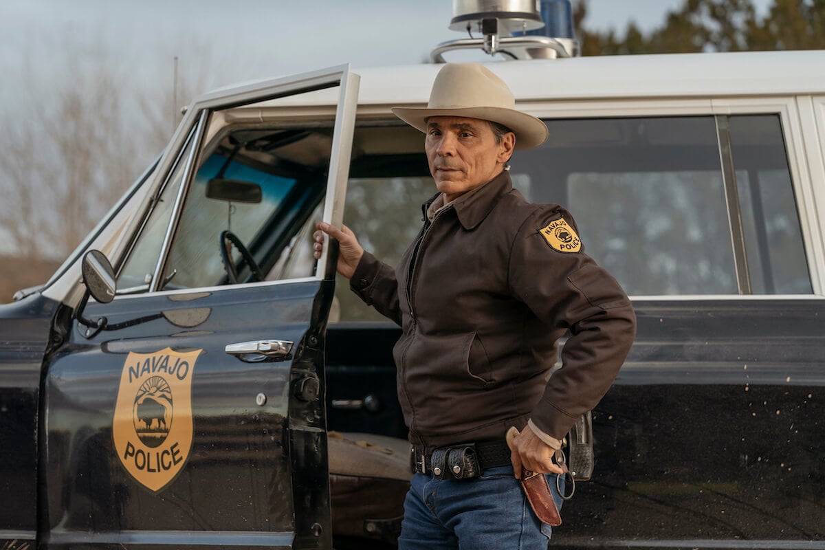 Zahn McClarnon as Joe Leaphorn, standing in front of the open door of a police car in 'Dark Winds' Season 2
