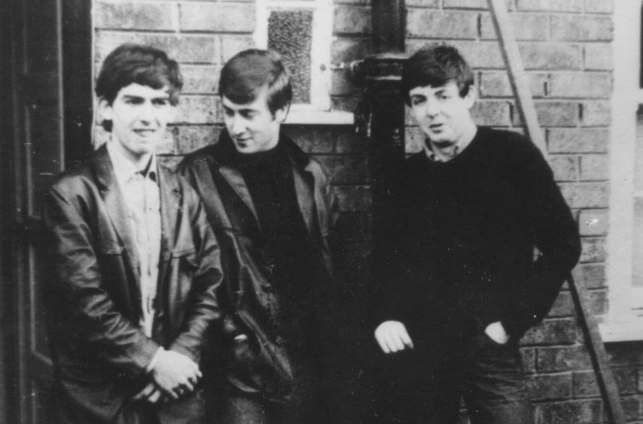 A black and white picture of George Harrison, John Lennon, and Paul McCartney posing in front of a brick building.