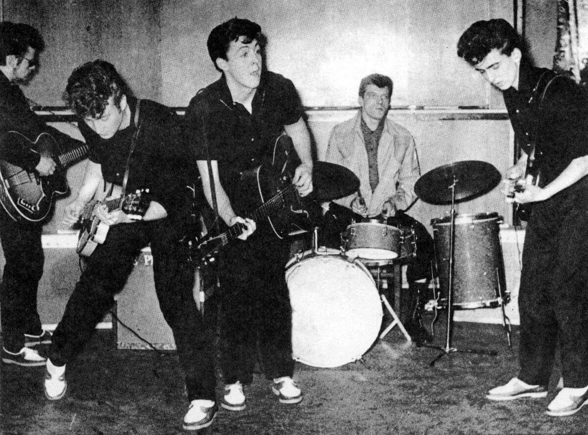 A black and white picture of Stu Sutcliffe, John Lennon, Paul McCartney, Johnny Hutch and George Harrison performing on a stage.