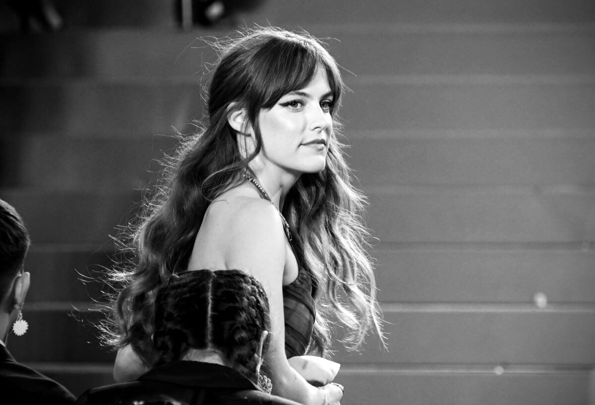 A black and white picture of Elvis' granddaughter Riley Keough standing at side profile on the stairs.